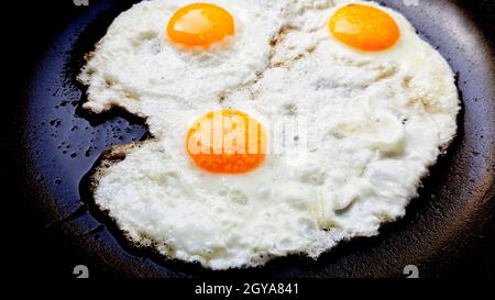 Three free range fried eggs in a hot non stick frying pan. Stock Photo