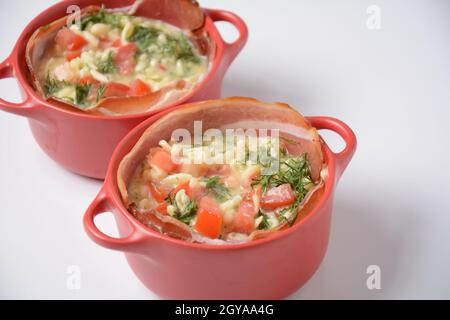 Proсess of cooking Omelette  with bacon, grated parmesan and greens. Raw beaten egg yolks  with ingredients in ceramic cocotte Stock Photo