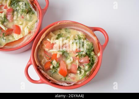 Proсess of cooking Omelette  with bacon, grated parmesan and greens. Raw beaten egg yolks  with ingredients in ceramic cocotte Stock Photo