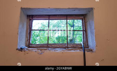 A rectangular basement window is tightened with a metal mesh and a grill. Technical window in the wall of an old gray building Stock Photo