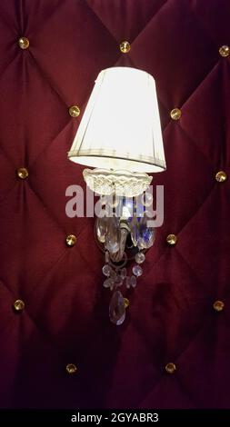 Retro bedroom lamp with a red wall. Antique sconces hanging on a wall of textile with buttons Stock Photo