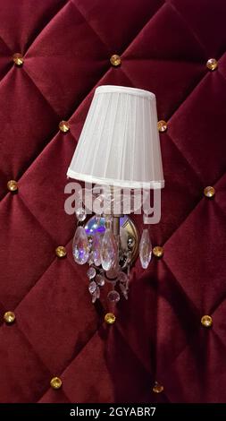 Retro bedroom lamp with a red wall. Antique sconces hanging on a wall of textile with buttons Stock Photo