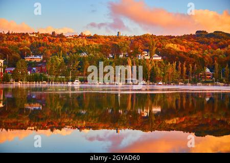 Sail boats and other boats docked on a shoreline bathed in fall colors and with a river reflecting the scene Stock Photo