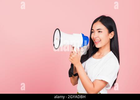 Portrait of happy Asian beautiful young woman teen confident smiling face holding making announcement message shouting screaming in megaphone, studio Stock Photo