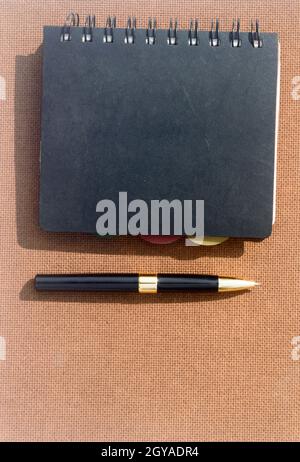A notebook and a pen on Brown Color Hard cork board. High angel view. Vertical. Business Education background. Copy space room for text. Stock Photo
