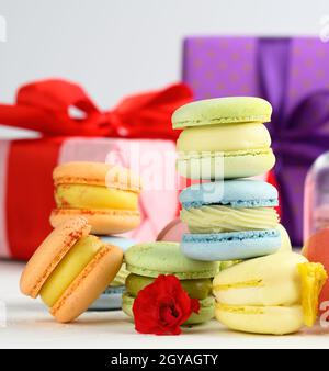 baked macarons with different flavors and rosebuds on a white background, behind gift boxes, close up Stock Photo