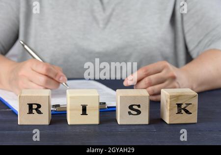 inscription risk on wooden cubes and a woman sitting at the table. Business deal analysis concept, planning Stock Photo
