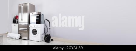 Set Of Household Kitchen Electronics Appliances On Reflective White Floor Against Wall Stock Photo