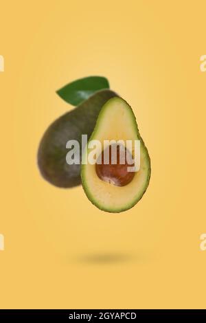 Fresh ripe whole and sliced avocado flying in air isolated on yellow background. Healthy food, diet, tropical exotic fruit, trendy food product. Creat Stock Photo