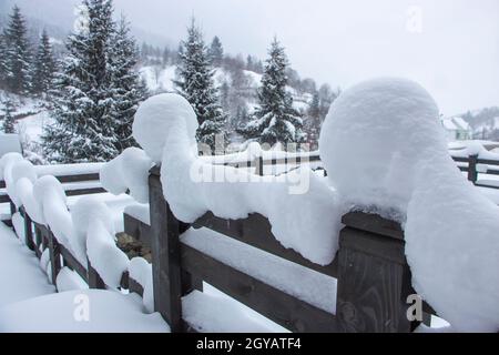 Snow on a wooden fence near the house in the mountains between Christmas trees and spruces. Selective focus Stock Photo