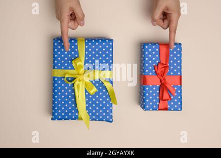 two gift boxes wrapped in a silk ribbon on a beige background, female fingers indicate choice Stock Photo