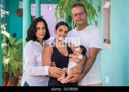 Photo of a group of people standing. Composed of a baby in the arms of a young woman, a man and a woman Stock Photo