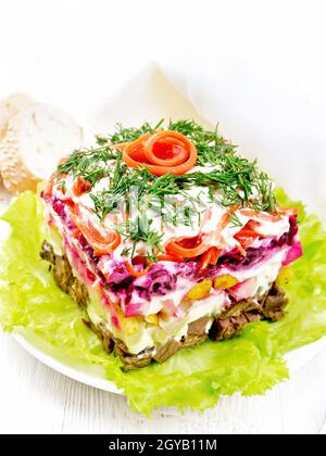 Puff salad with beef, potatoes and beets, pears, Korean spicy carrots, seasoned with mayonnaise and garnished with dill on a green lettuce in a plate, Stock Photo