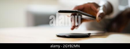 Man Charging Smartphone Using Wireless Charging Pad At Home Stock Photo