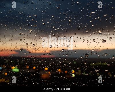 Raindrops on the window right after sunset. City lights and beautiful sky at the background. Stock Photo