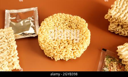 circle of instant noodles with raw spices on a plain brown background. Sprinkle dry Chinese or Korean vermicelli with salt and spices before pouring b Stock Photo