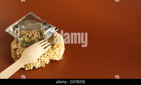 Raw instant noodles in the shape of a circle with a wooden fork and aromatic seasonings and butter. pasta, for the preparation of which it is enough t Stock Photo