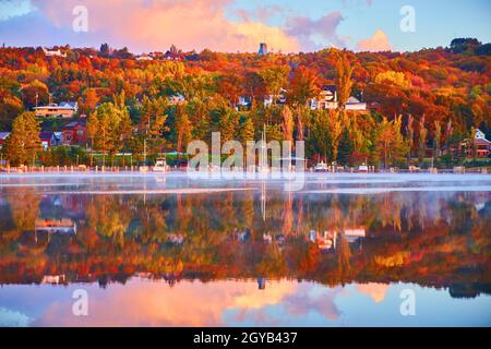 Fall at a harbor with pink, purple, and yellow clouds in a blue sky with a nearly glassy river surface and boats Stock Photo