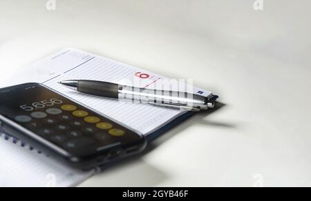 Ballpoint pen on a ring binder with blank pages and a mobile phone with the calculator running. Selective focus. Stock Photo
