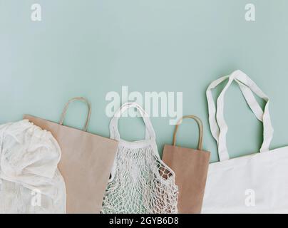 Flat lay with eco white craft paper bags and net bags on green background with copy space empty advertising area. Packaging template mock up. Delivery Stock Photo