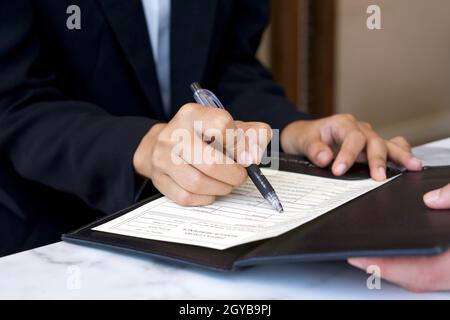 Closeup hotel manager hand holding pen, pointing at guest registration document. Stock Photo