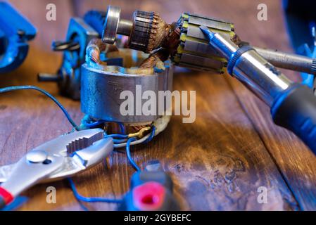Power tool repair. Details of an electrical appliance and tools for repair on a wooden table in a repair shop. A foreman repairs a power tool using a Stock Photo