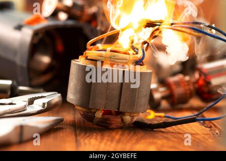 Burning wires on the details of an electrical appliance on a wooden table in a repair shop. Power tool repair. Stock Photo