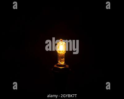 Glow of a halogen bulb in the dark. Light of an electric halogen bulb in the dark. Electric light source. Electric lighting. Electricity. Black backgr Stock Photo