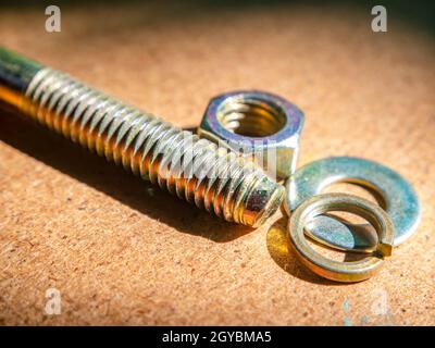 Bolt and nut on a wooden table macro photo. Iron bolt. Washer under the nut. Locksmith material. Wooden background. Macro photography. Background imag Stock Photo