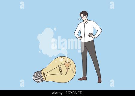 No idea, challenge and crisis concept. Young frustrated Businessman standing looking at fallen broken light bulb feeling problems in creativity Stock Photo