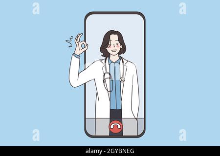 Virtual doctor and online health concept. Young smiling woman doctor in white uniform standing showing ok sign from smartphone screen eHealth and tele Stock Photo