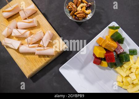 Turkey ham rolls, diced fruit paste, and nuts on a black surface Stock Photo