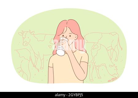Fresh cow farm milk concept. Small girl standing and drinking fresh organic dairy milk from glass or bottle on farm with eating cows at background. He Stock Photo