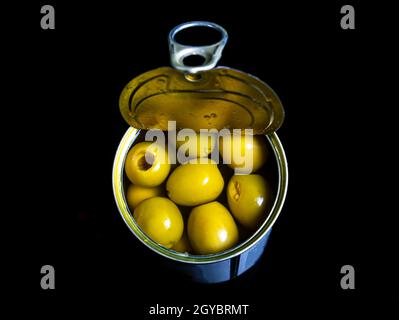 Green olives in a tin can on a black background. Green olive fruits. Olives berries. Olive fruits. Vegetables and fruits. Food photo. Canned food. Sna Stock Photo