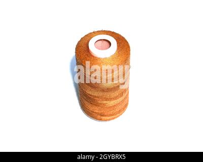 A large spool of brown sewing thread on a white background. Spool of thread for sewing. Clothing repair. Tailor and seamstress tool. White background. Stock Photo
