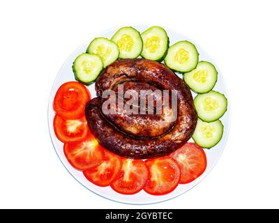 Smoked meat sausage on a plate with tomatoes and cucumbers on a white background. Smoked sausage. Pork meat. Chopped vegetables. Red tomato. Green cuc Stock Photo