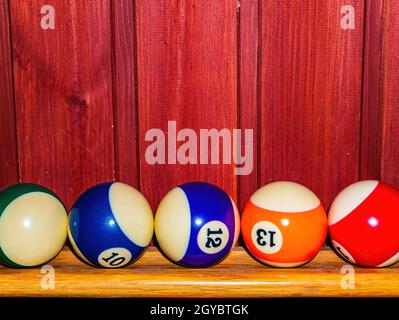 Colored billiard balls on a wooden shelf. Billiard ball. Wooden shelf. Numbered balls. Gambling. Sports game. Leisure activities. Business. Background Stock Photo