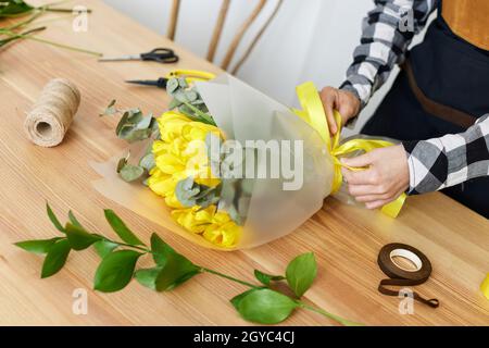 Florist woman makes a bouquet of fresh yellow tulips. Floral design studio Stock Photo