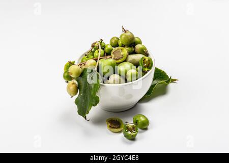 Ripe Actinidia arguta or kiwi in a bowl isolated on white background. Branches of fresh fruits with green leaves, mockup, template Stock Photo