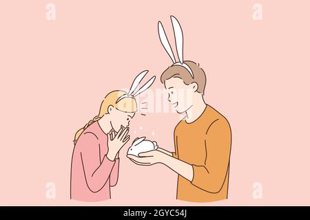 Funny cute present for girl concept. Young smiling boy cartoon character wearing rabbit ears giving white small rabbit gift for his surprised happy gi Stock Photo