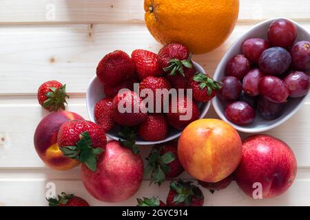 Health and life benefits of strawberries, grapes, nectarines, oranges; high angle photo of fruit on traditional wooden background Stock Photo