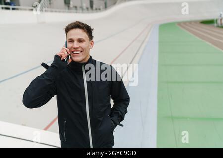 Smiling male athlete standing at the stadium and talking on mobile phone Stock Photo