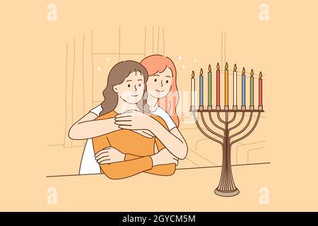 Celebrating holy Hanukkah holiday concept. Two happy Jewish sisters sitting hugging looking at beautiful menorah candelabra glowing on eight day of Ha Stock Photo