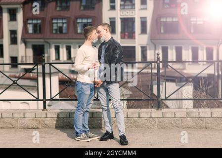 Young gay couple wearing medical mask, hugging and kissing at city. Stock Photo