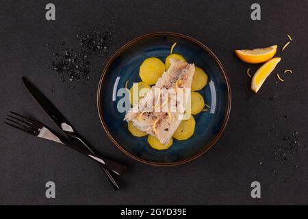 Grilled fish fillet served with potatoes on plate over black background. Culinary eating. Stock Photo