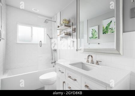 A bathroom with a white vanity cabinet, granite countertop, and a shower lined with large herringbone tiles. Stock Photo