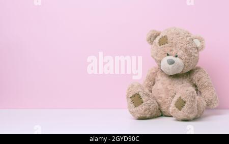 brown teddy bear with patches sits on a white table, pink background, copy space Stock Photo