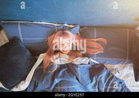 Cheerful lady lies under soft duvet in comfortable bed with soft pillows Stock Photo