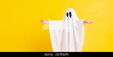 Funny Halloween Kid Concept, Closeup a little cute child with white dressed costume halloween ghost scary, studio shot isolated on yellow background Stock Photo