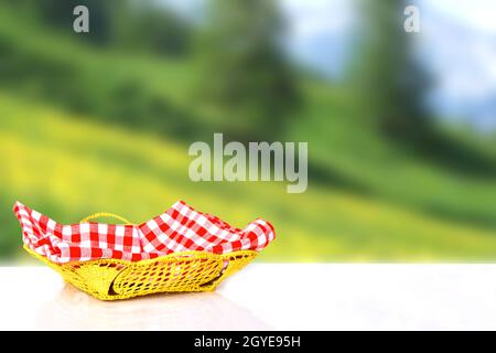 Empty basket with red checkered napkin on white table over abstract blurred natural sunny landscape background. Template for your product display mont Stock Photo